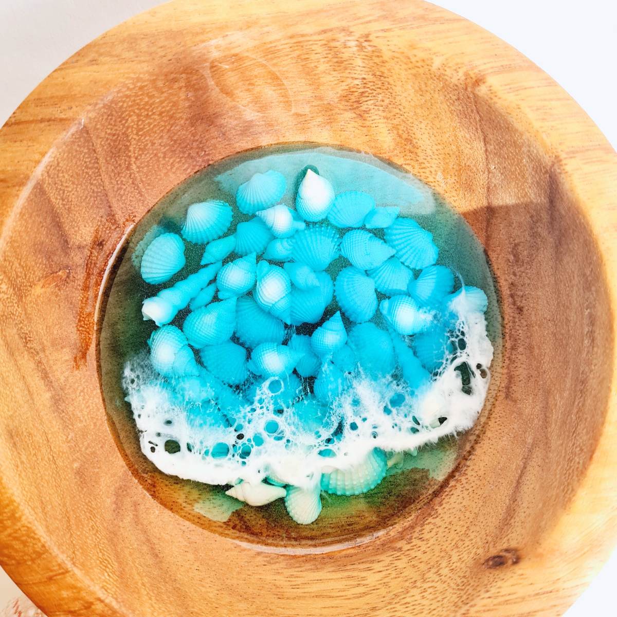 close up of a wooden bowl with resin ocean art and shells inside on a white background