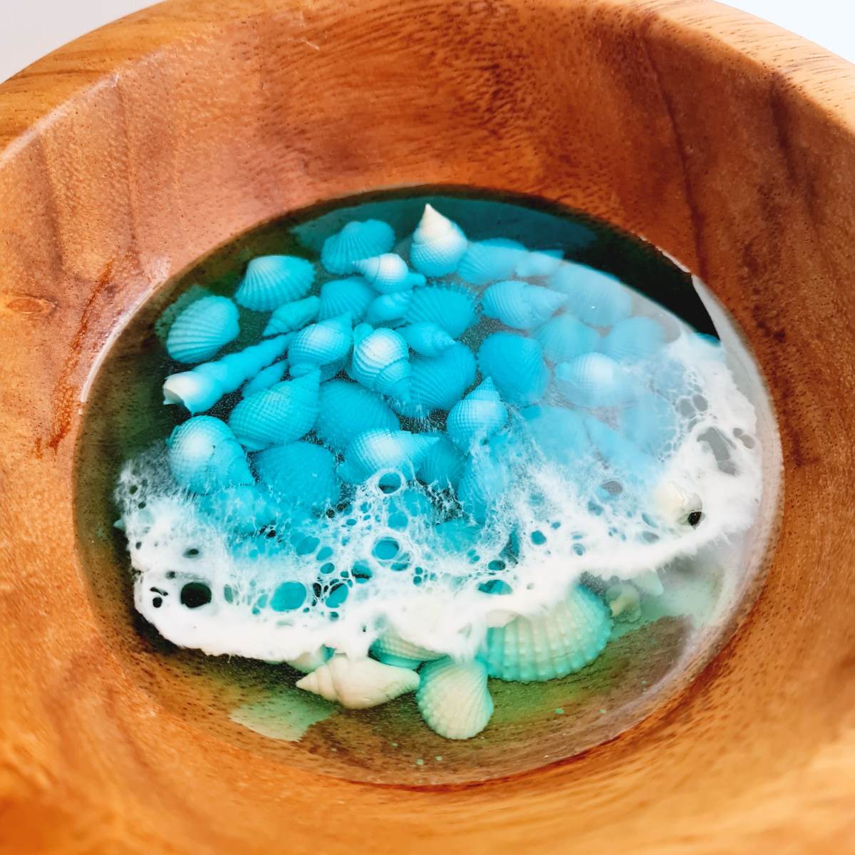 wooden bowl with resin ocean art and shells inside on a white background