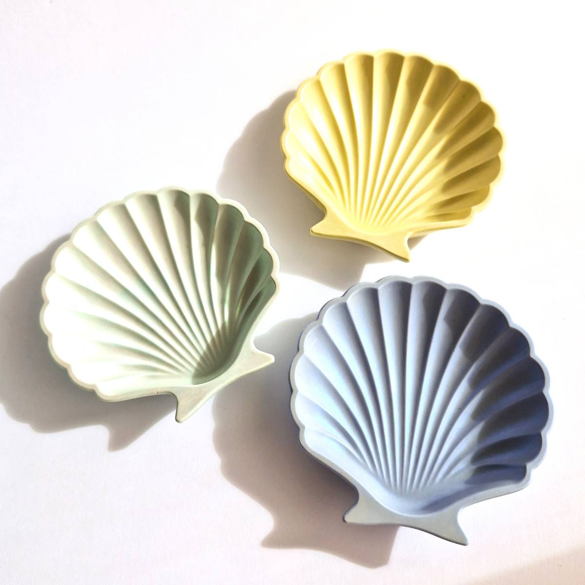 three shell trinket dishes in blue, green and yellow on a white background