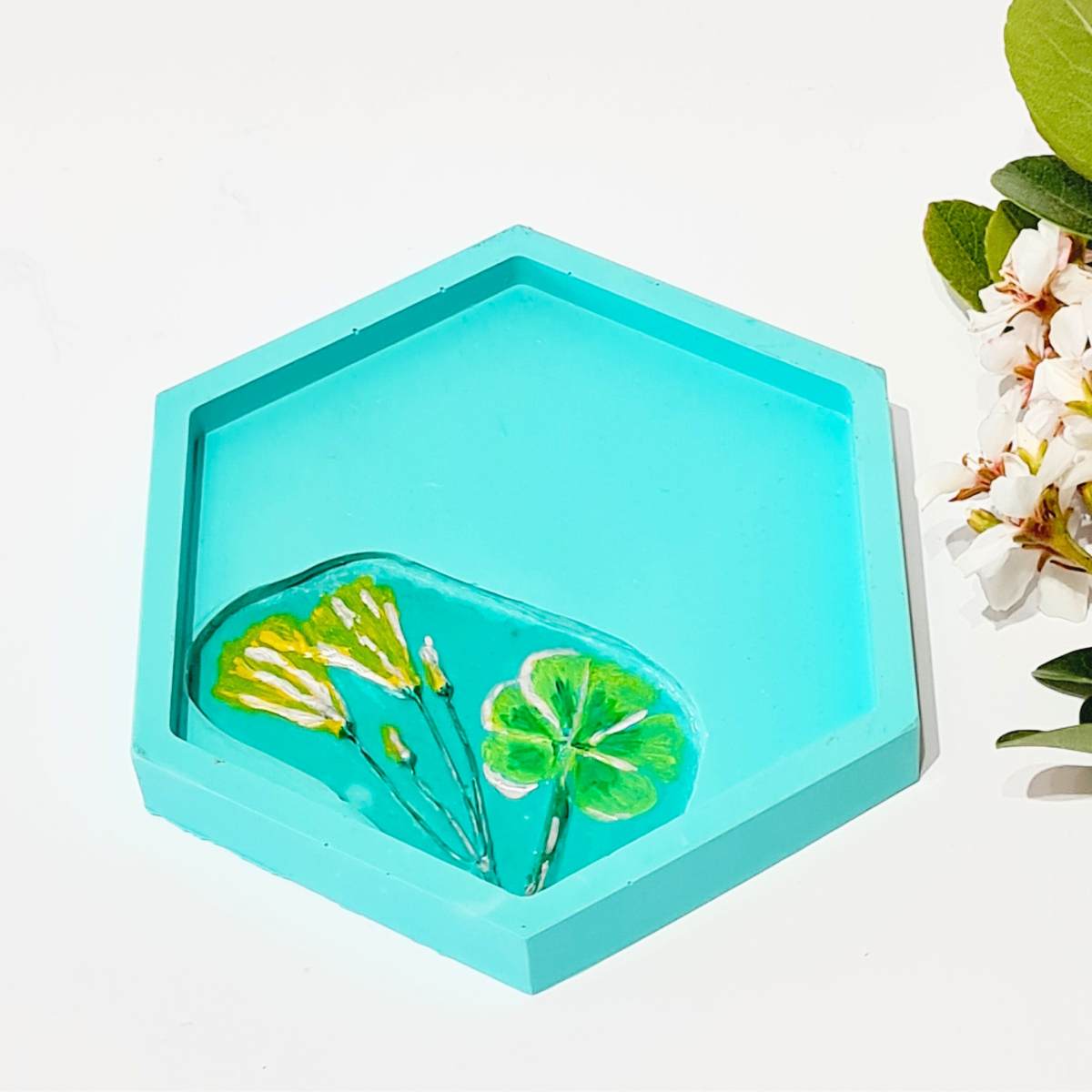 a hexagon shaped turquoise ring dish with flower imprint on a white background 