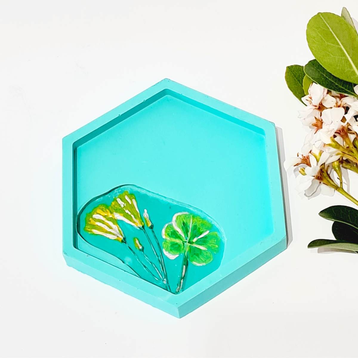 a hexagon shaped turquoise ring dish with flower imprint  on a white background 