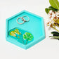 a hexagon shaped turquoise ring dish with flower imprint and two rings in it, on a white background 