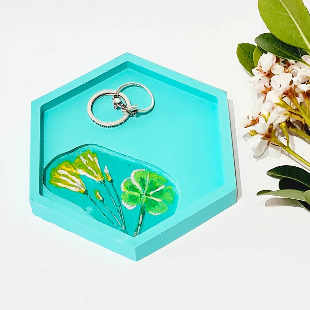 a hexagon shaped turquoise ring dish with flower imprint and two rings in it, on a white background 