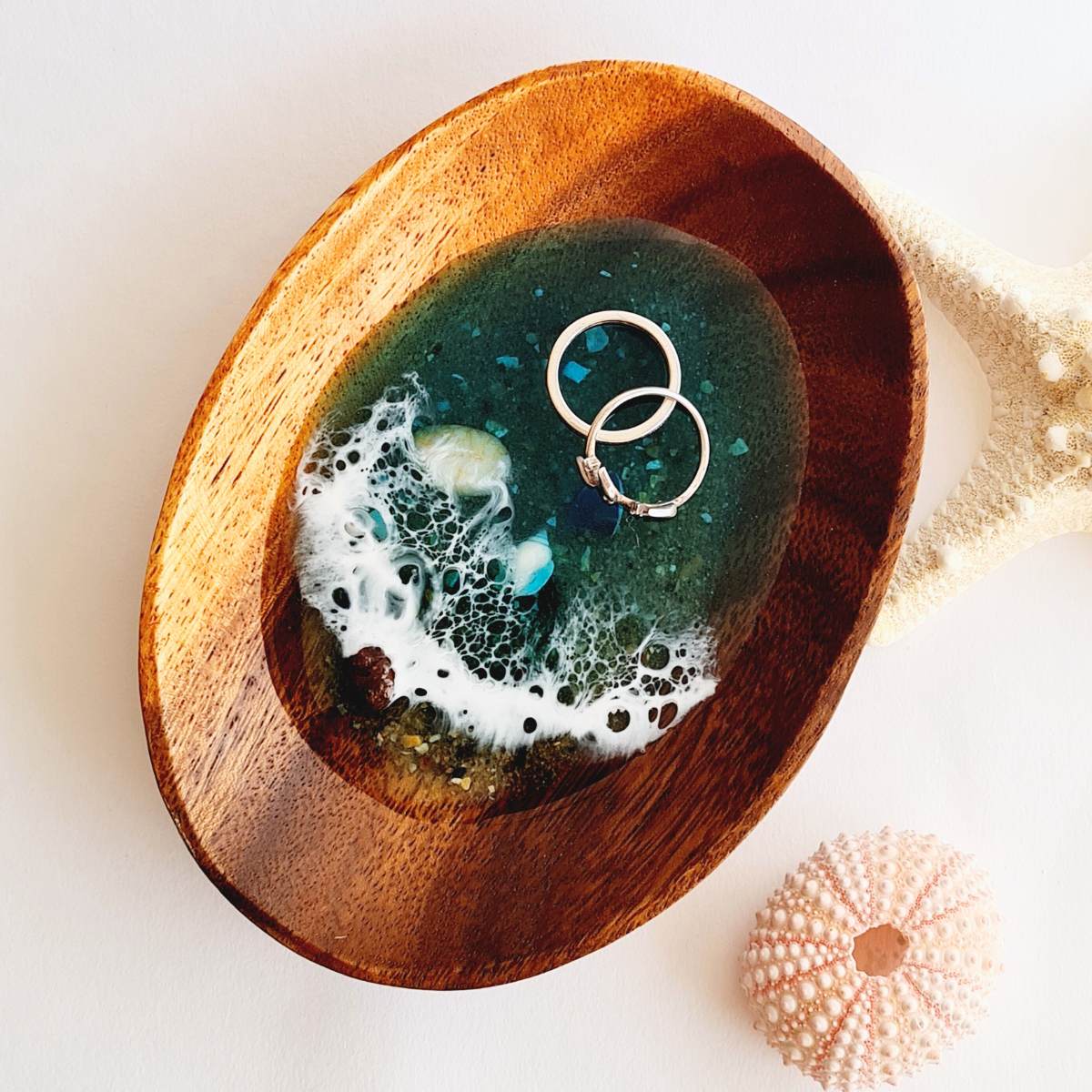 a wooden jewellery dish with resin ocean art with two rings on it on a white background