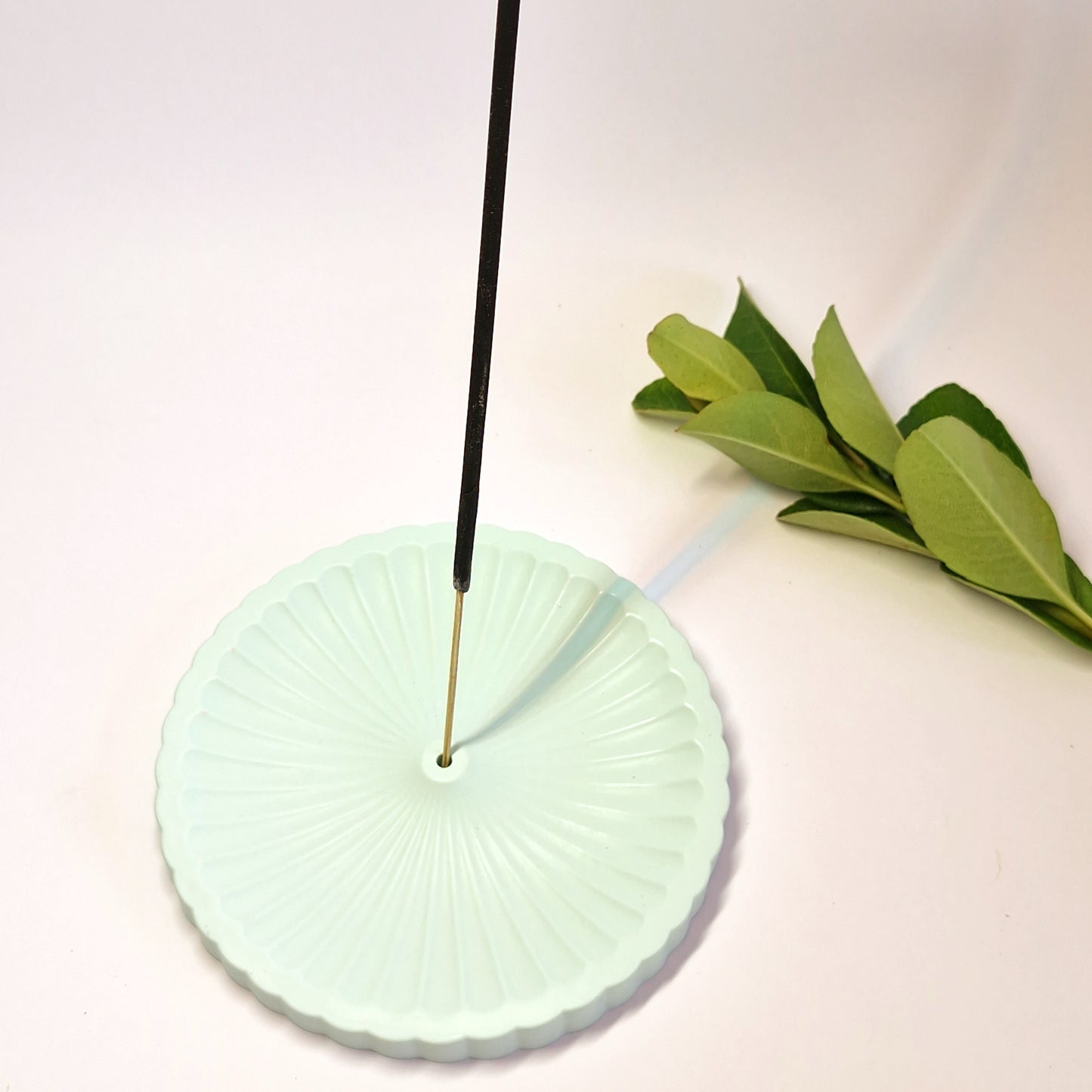 a light green incense holder with an incense on a white background with a green leaf