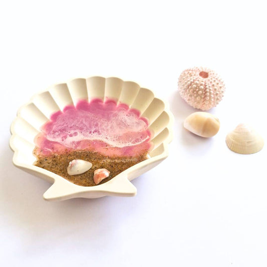 a white shell shaped ring dish with pink  ocean resin art on a white surface