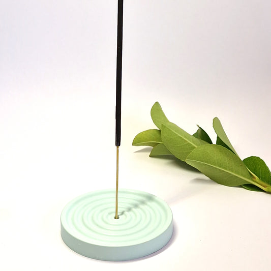 a light green small incense holder with an incense stick in it on a white surface